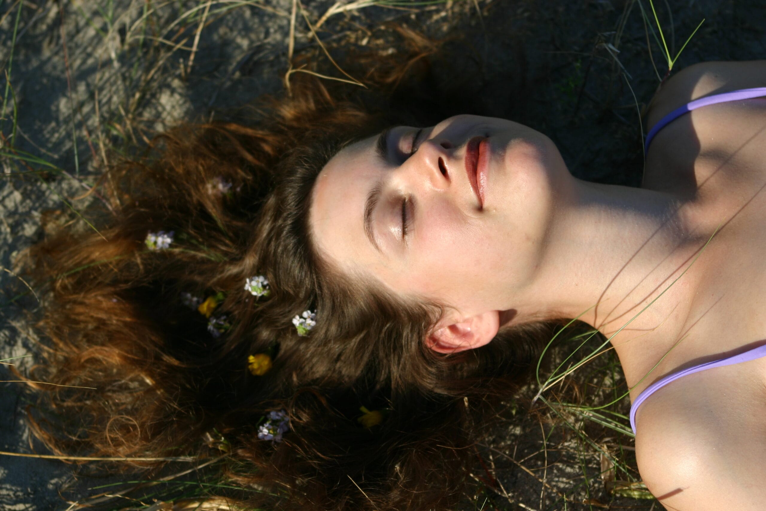 Vrouw met bloemen in haar, liggend op het strand, cursus huid haar en nagels
